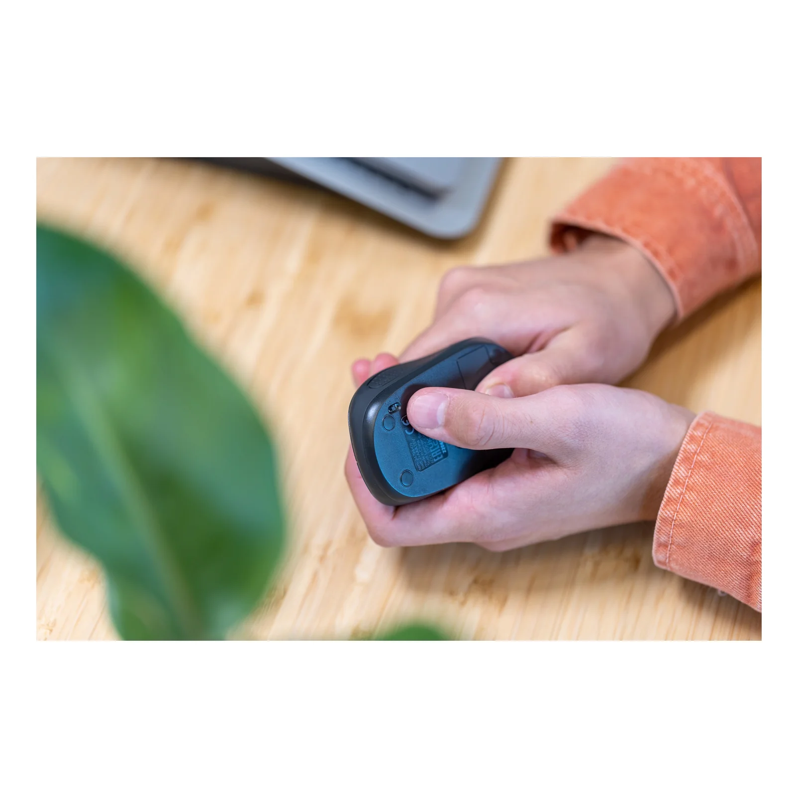 Main tenant une souris compacte foncée vue du dessus, bureau en bois
