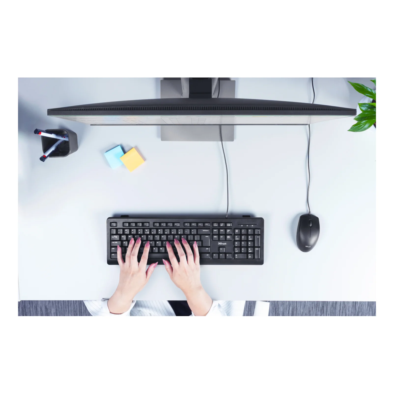 Vue aérienne d'usage, mains sur le clavier devant un écran incurvé, souris noire à droite