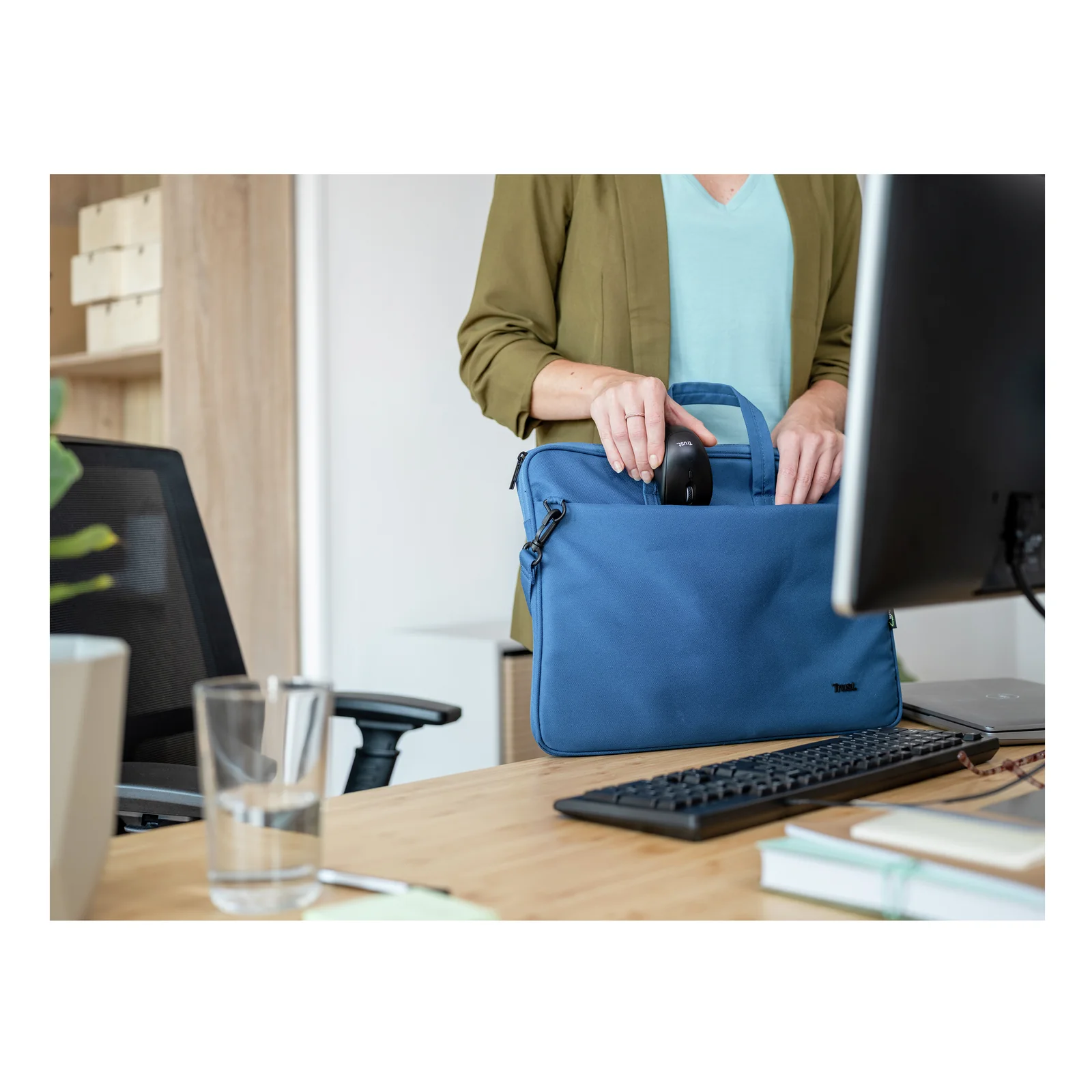 Femme tenant un sac bleu dans un bureau avec ordinateur en arrière-plan