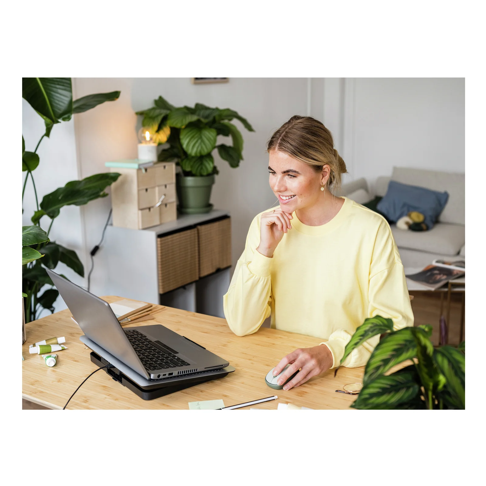 Femme en pull jaune utilisant la souris Trust Yvi+ verte devant un ordinateur portable sur un bureau blanc
